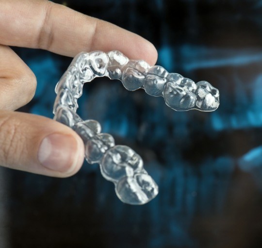 Person holding clear aligner in front of dental x rays