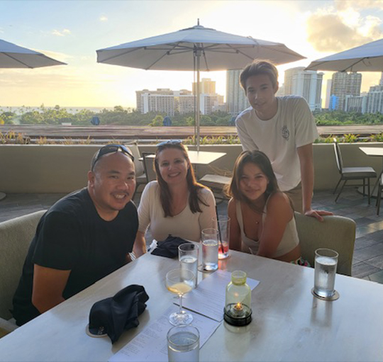 Doctor Wong with his family at outdoor table at restaurant with city skyline in background