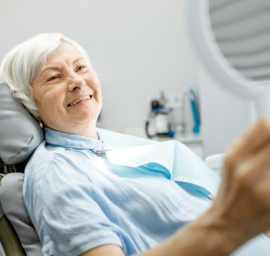 Senior dental patient looking at her smile in mirror