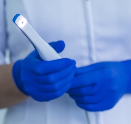 Gloved hands holding a thin white intraoral camera