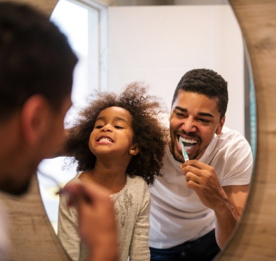 Man brushing his teeth next to his young daughter