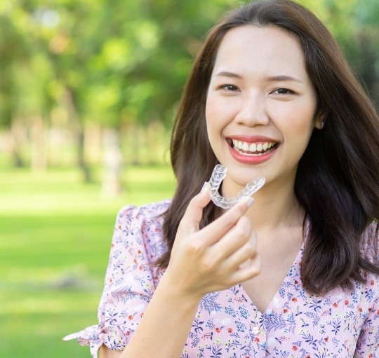 Smiling woman holding Invisalign clear aligner in Honolulu