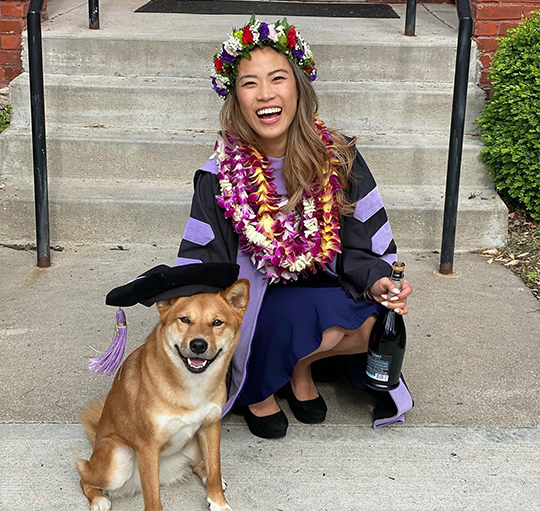 Doctor Koyanagi in her dental school graduation gown placing her cap on her dog