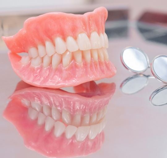 Set of full dentures resting on table next to two dental mirrors