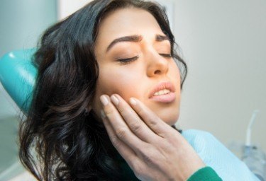 Woman in dental chair holding her cheek in pain